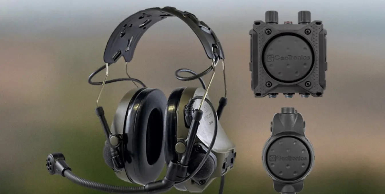 An image of an intercom system. The capability includes a headset with a microphone attached to it, and two items that appear to be receivers. The equipment are painted dark green and gray.