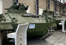 Two Marder 1A3 Infantry Fighting Vehicles are seen displayed inside a warehouse-like building. The vehicles are painted dark green.
