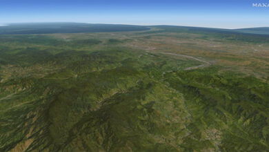 A shot of a land mass generated by Precision3D Data Suite by Maxar Intelligence. The computer-generated image shows a relatively flat and green landscape with small mountains. The background is a clear blue sky.