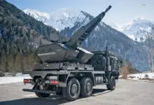 A Skynex air defense system is seen propped up on the back of a six-wheel truck. The capability's turret is pointed northwest. The background is a scenic view of a snowy mountain range.