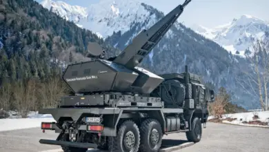 A Skynex air defense system is seen propped up on the back of a six-wheel truck. The capability's turret is pointed northwest. The background is a scenic view of a snowy mountain range.
